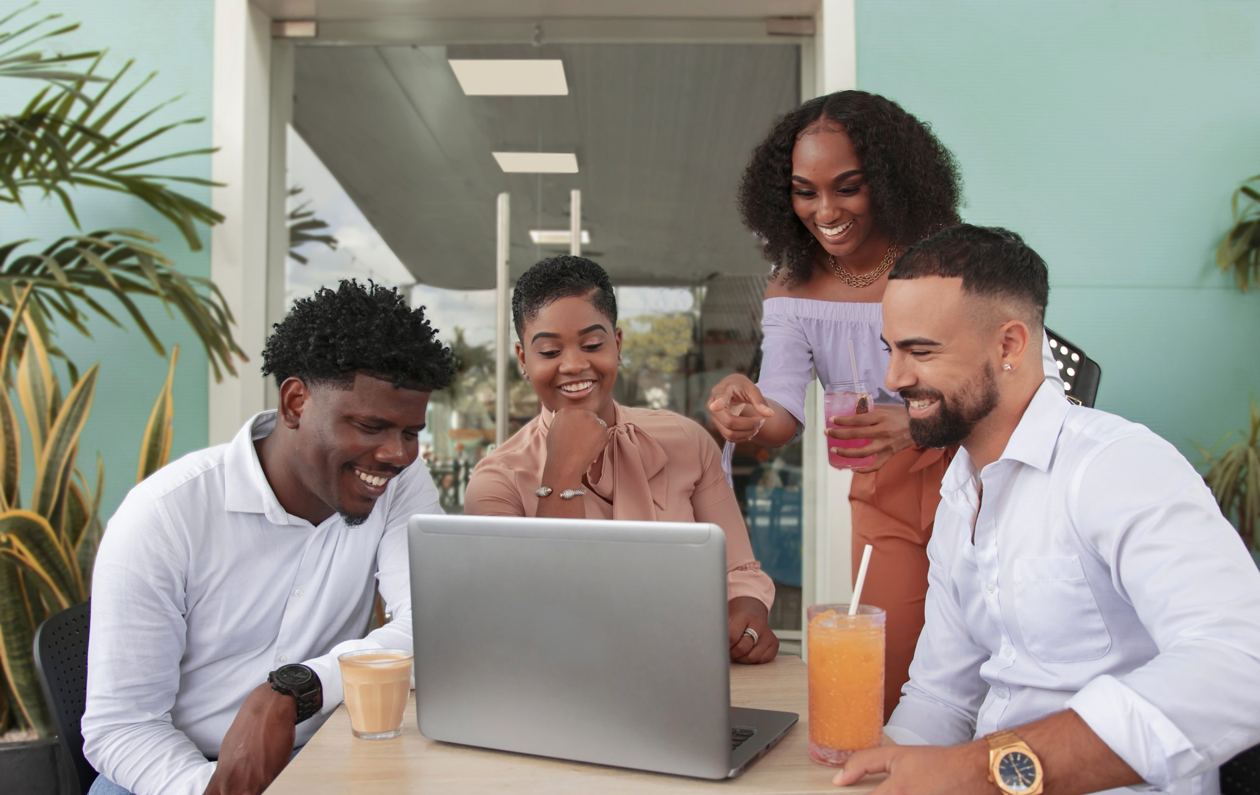 Four people having drinks at a table while looking at a laptop
