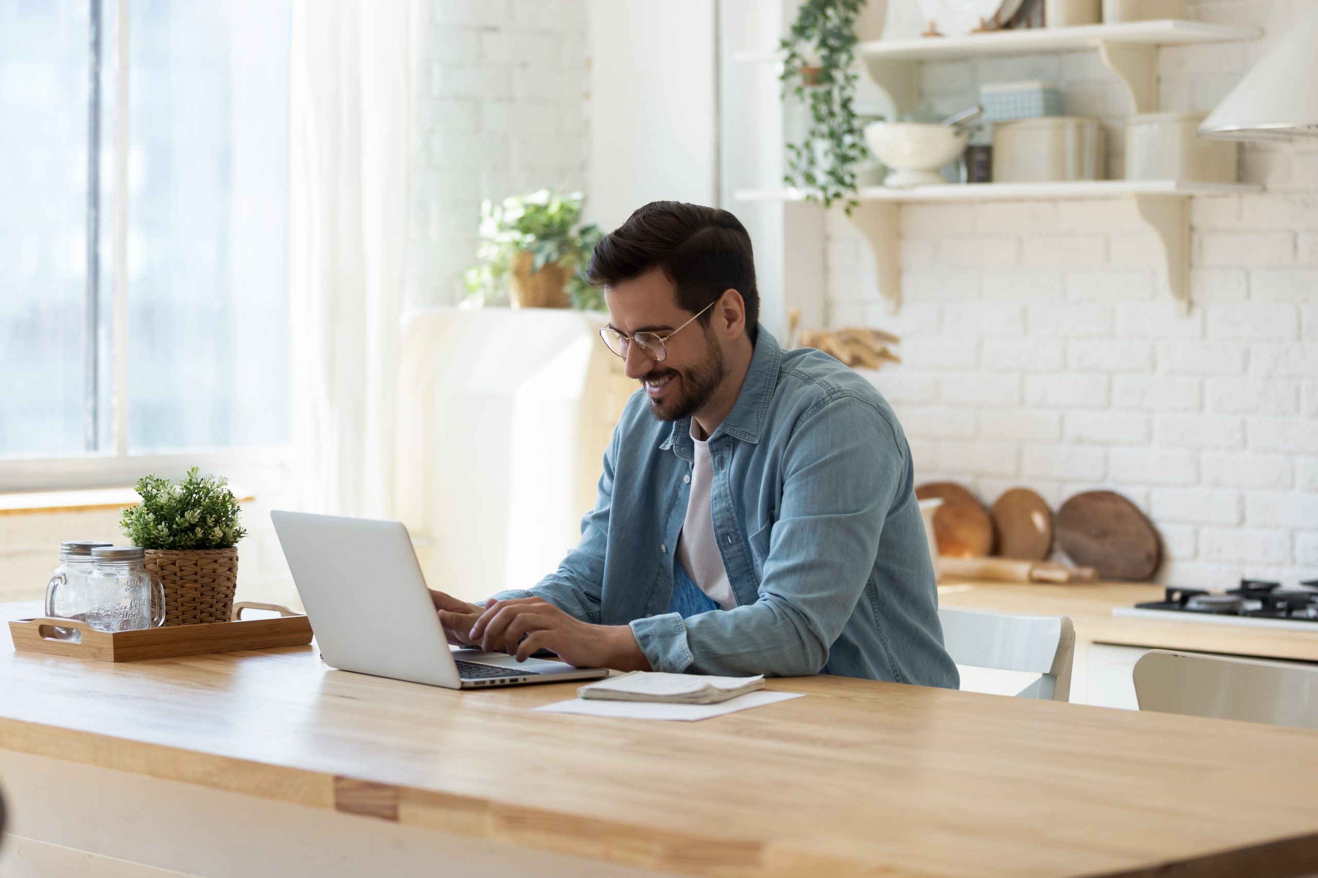 Man sitting in the kitchen on a table typing on his laptop