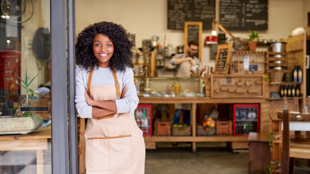 Woman with apron standing in the doorway of a coffee bar and smiling